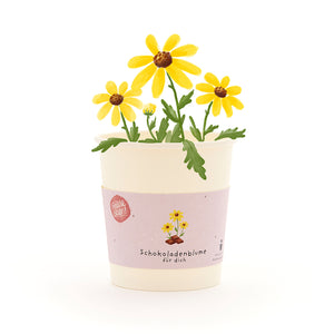 Becher mit gelben Schokoladenblumen und grĂŒnem Blattwerk, Etikett mit Aufschrift âSchokoladenblume fĂŒr dichâ.