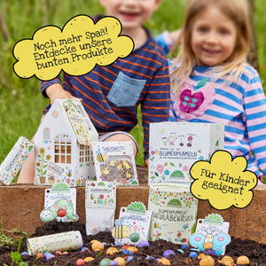 Zwei Kinder sitzen im Garten hinter einer Auswahl bunter, kindgerechter Blumensamen-Produkte und Verpackungen, die für Naturabenteuer und kreatives Spielen werben.