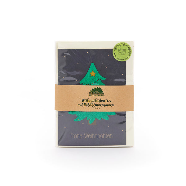 Weihnachtskarte mit grÃŒnem Weihnachtsbaum und Stern, in einer Verpackung mit braunem Papierband und der Aufschrift "Weihnachtskarten mit Wildblumensamen", daneben ein grÃŒner Sticker mit "Pflanz mich".