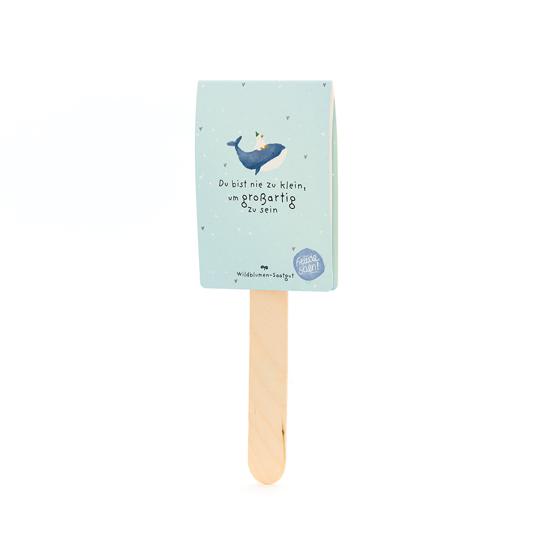 Holzstäbchen mit hellblauem Papieranhänger, darauf ein Wal mit Partyhut und der Text „Du bist nie zu klein, um großartig zu sein“.