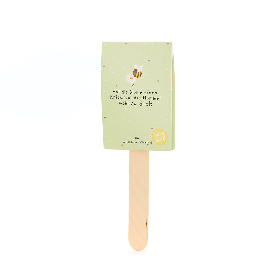 Grüner Papieranhänger mit einem Bienenmotiv und dem Spruch „Hat die Blume einen Knick, war die Hummel wohl zu dick“ auf einem Holzstab.