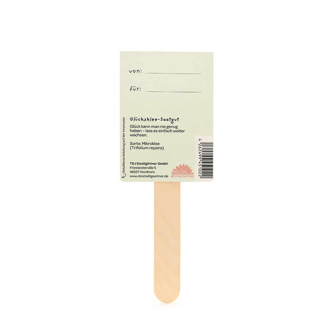 Rückseite eines Glücksklee-Saatgut-Sticks mit Beschriftungsfeldern „von“ und „für“, sowie Textinfos und Barcode auf hellem Hintergrund.