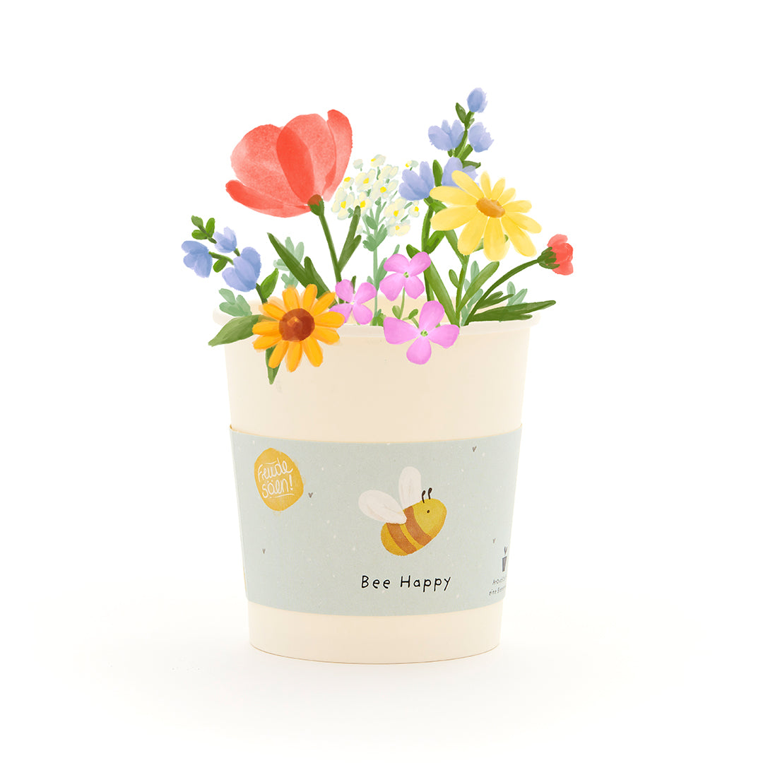 Blumentopf mit bunten Blumen und einer Biene auf dem Etikett mit der Aufschrift "Bee Happy".