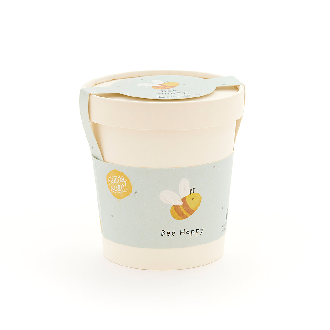 Beiger Becher mit hellblauem Etikett, auf dem eine gezeichnete Biene und der Schriftzug "Bee Happy" zu sehen sind.