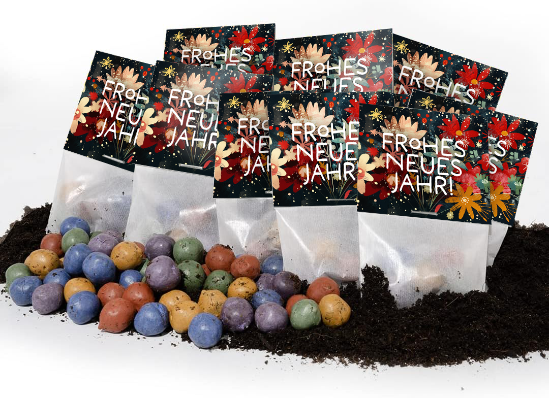 Mehrere bunte Samenbomben liegen auf Erde vor Tütchen mit der Aufschrift "Frohes neues Jahr" und Blumenmuster.
