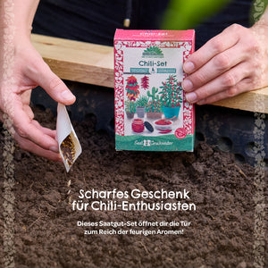 Person hält eine Chili-Saatgut-Box und sät Samen in Erde.