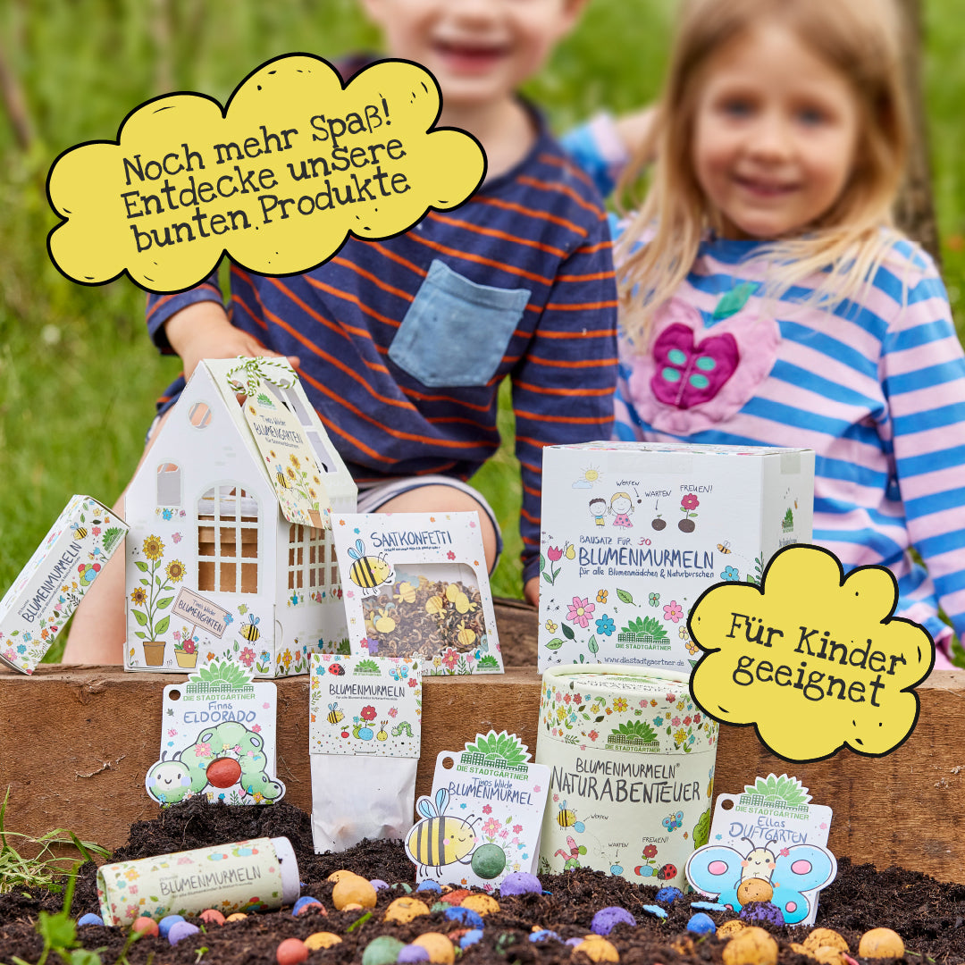 Zwei Kinder sitzen im Garten hinter einer Auswahl bunter, kindgerechter Blumensamen-Produkte und Verpackungen, die für Naturabenteuer und kreatives Spielen werben.