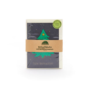 Weihnachtskarte mit grünem Weihnachtsbaum und Stern, in einer Verpackung mit braunem Papierband und der Aufschrift "Weihnachtskarten mit Wildblumensamen", daneben ein grüner Sticker mit "Pflanz mich".