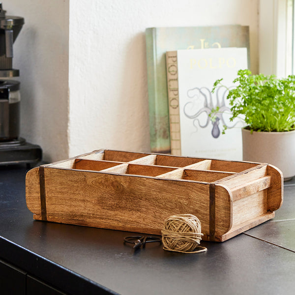 Holzkiste auf einer Arbeitsplatte mit Garnknäuel und Pflanze im Hintergrund.