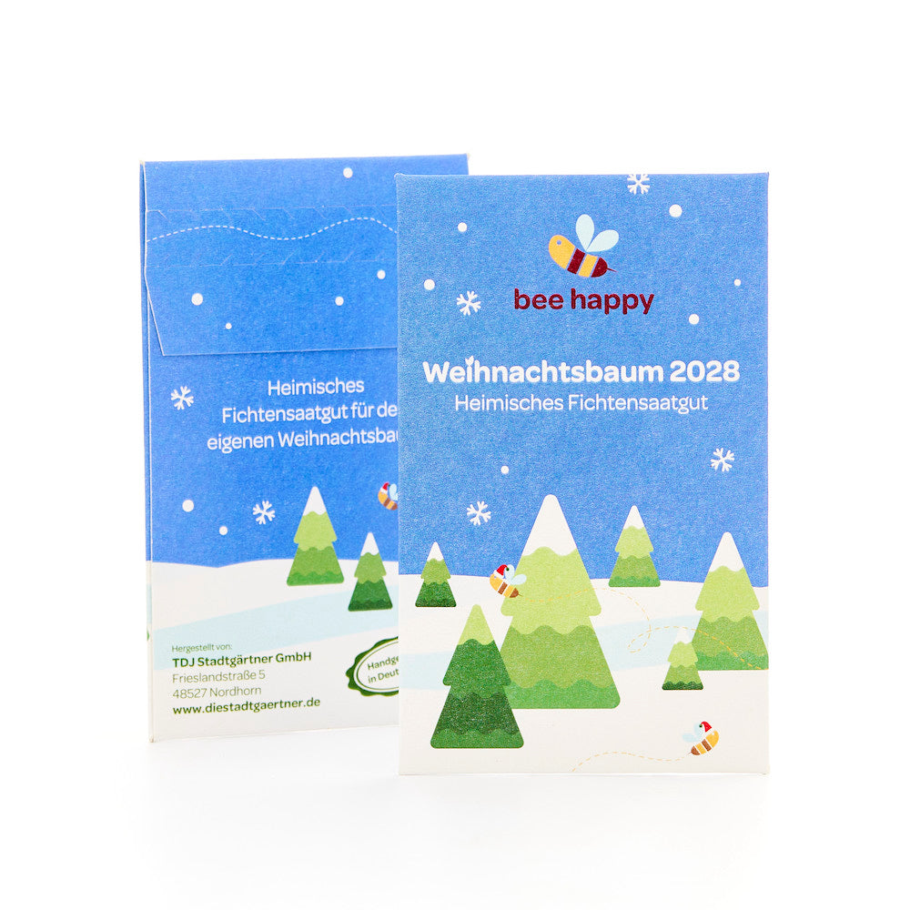 Zwei blaue Verpackungen mit weihnachtlichem Design, Tannenbäumen, Schneeflocken und einer Biene, beschriftet mit "Weihnachtsbaum 2028 Heimisches Fichtensaatgut" und dem Slogan "bee happy".