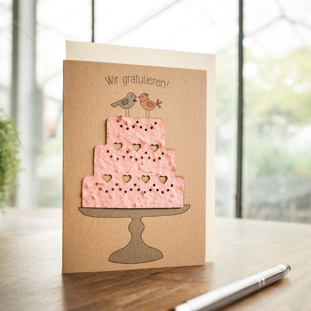 Glückwunschkarte mit rosa Torte und zwei Vögeln, darüber der Text "Wir gratulieren!"
