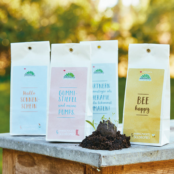 Verpackte Samenbomben mit lustigen Sprüchen auf einem Steinsockel im Garten.